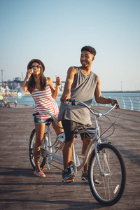混合的种族的夫妻在上双人自行车户外海边玩耍的肖像