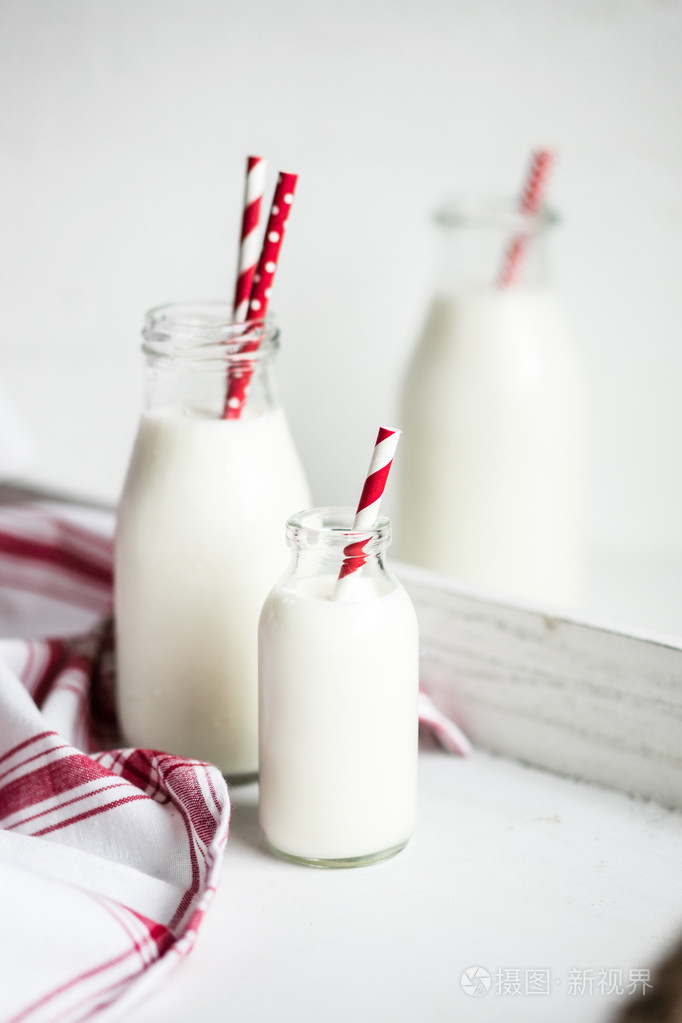白色的木制背景上的红色条纹吸管牛奶罐