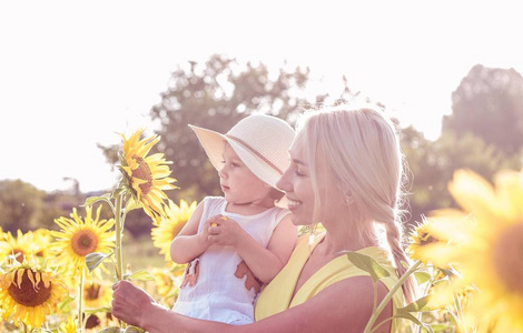 家庭沿着夏季开花字段。幸福的母亲和女儿在阳光下。夏天。向日葵