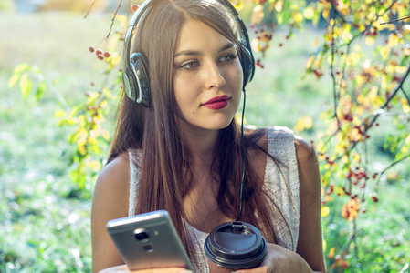 在阳光明媚的日子里, 你的手机里戴着耳机听音乐的女人。有声观与学生教育