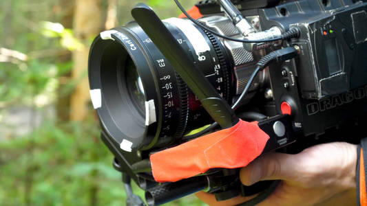 男子拿着照相机拍摄一部电影在森林里。昂贵的相机，在树林里的电影