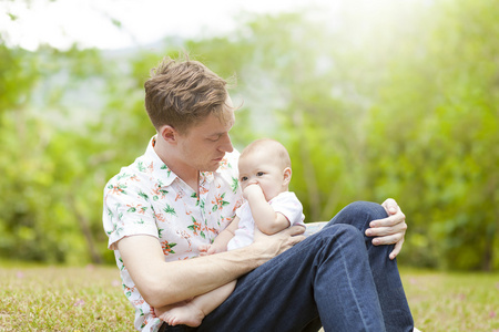 他的父亲坐在户外的春天 p 的绿色草地上的婴儿