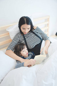 快乐家庭年轻亚洲慈母教她的女儿到床上时间的故事书