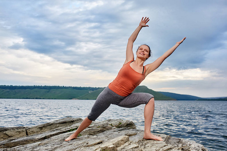 年轻女人站在石头上，练瑜伽在大河边