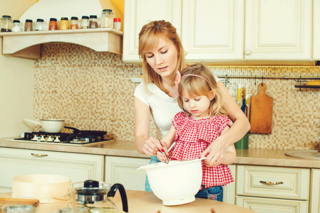 年轻的母亲和可爱的小女儿准备面团烘制饼干和乐趣在厨房里