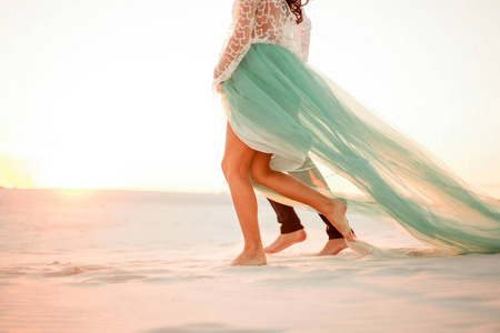新娘和新郎赤脚走在沙漠日落时分的双腿。Cl