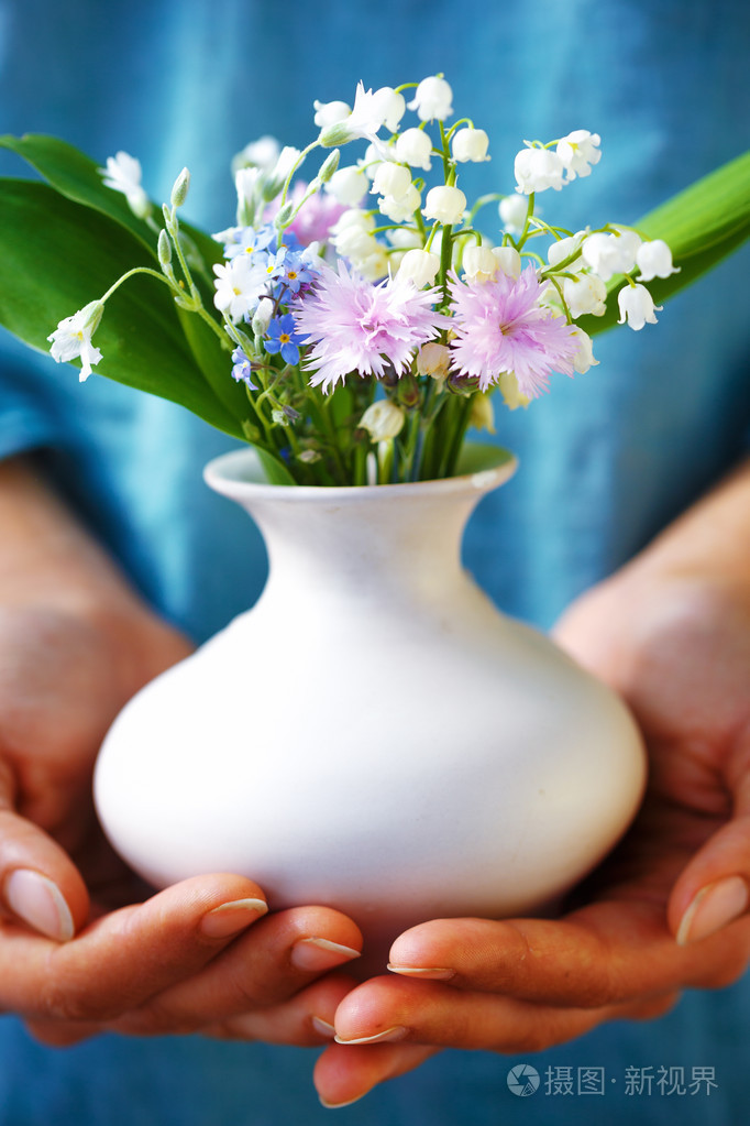 手持束花插在花瓶里的女人蓝色服装背景