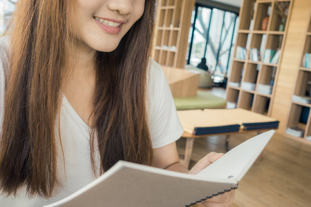 女学生在图书馆从一本书笔记。年轻的亚裔女子，坐在餐桌旁做中高校图书馆的工作分配。老式的影响风格图片