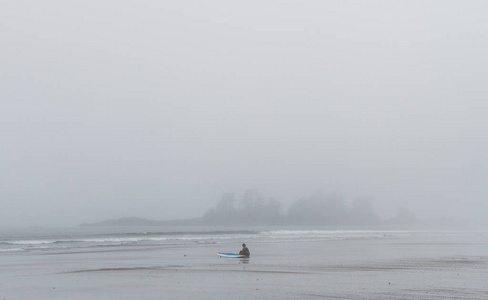 潜水服坐在雾期待着海洋的海滩上的冲浪者