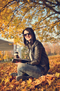 女孩与杯咖啡坐在叶在公园里