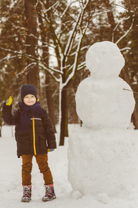 冬季活动的概念。快乐的男孩站在室外的雪人