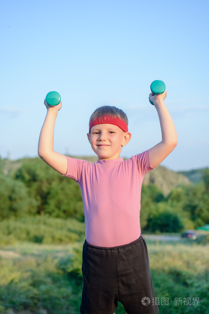 微笑的强壮男孩举起两个哑铃