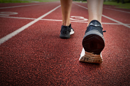 赛跑者脚在鞋上的赛马场特写上运行。女人健身慢跑锻炼入场概念