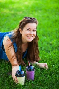 戴墨镜的年轻女子在绿色的草坪草地上喝多汁美味奶昔