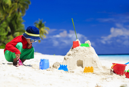 小男孩建设热带海滩上的堆沙堡照片