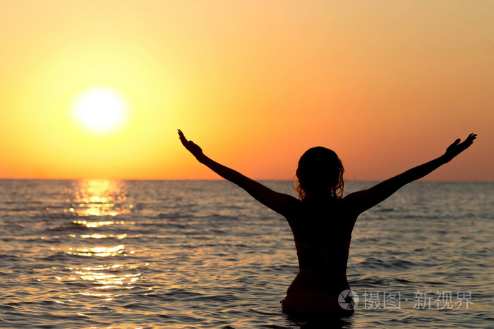 一个女孩穿着泳装在日出的海水中的剪影