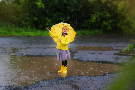 小小的女孩穿着黄色夹克和黄色靴子黄色雨伞在雨中。雨伞的女孩喜欢雨