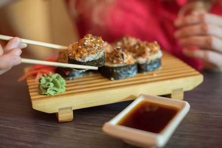 女孩吃日本食品保持寿司卷与木 chopsti照片
