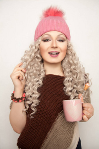 年轻漂亮的女人，穿着粉色的针织的帽子站在一起喝杯茶和触摸她的头发上分离出的白色背景
