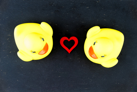 对孤立在黑色的黑板背景和红色心形之间，爱概念的黄色橡胶鸭子