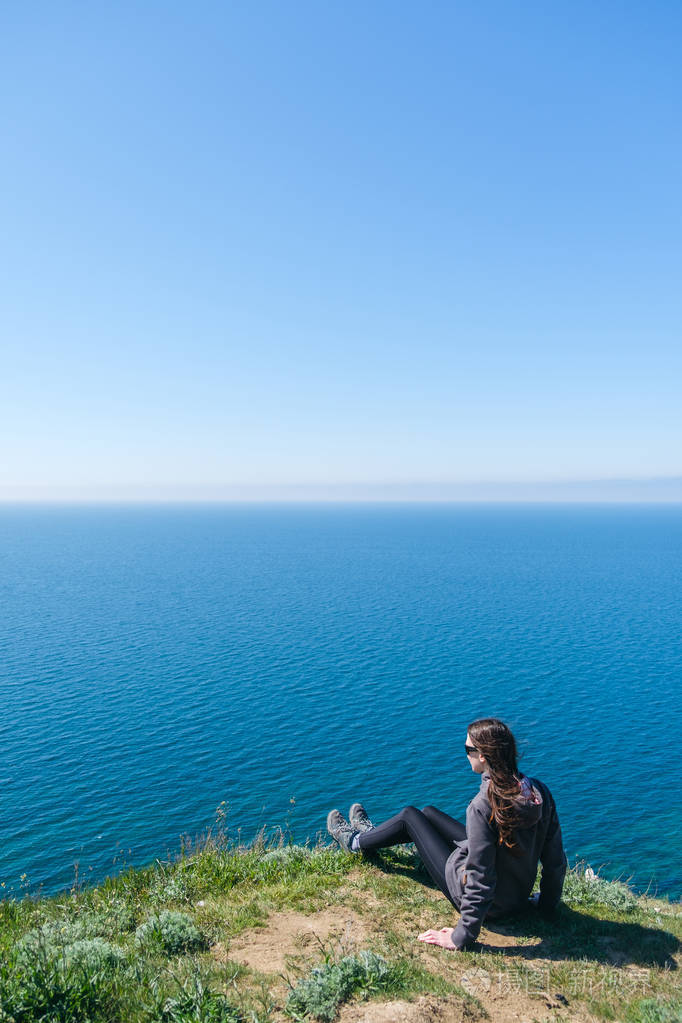 年轻的女人正坐在海边的悬崖上