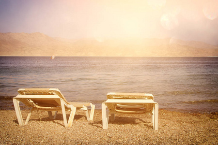 热带的海滩和两个贵妃椅在夕阳的光。夏天的旅游和度假概念