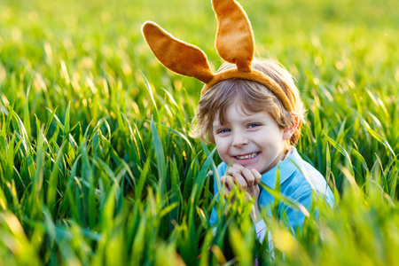 可爱的小男孩与复活节兔子耳朵玩在绿色鹅肝