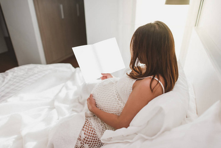 怀孕的女人躺在家里的床上看书