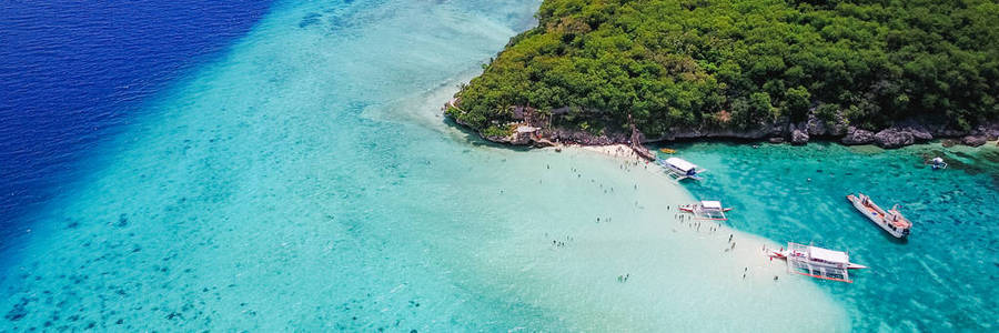 游客在美丽清澈的海水水落在奥斯洛布，菲律宾宿雾市附近的苏密隆碧海岛屿海滩游泳沙滩的鸟瞰图。彩色增强处理。全景横幅