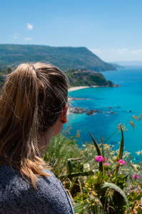 从后面看着大海蓝色地中海美丽卡拉布里亚海岸的金发女人