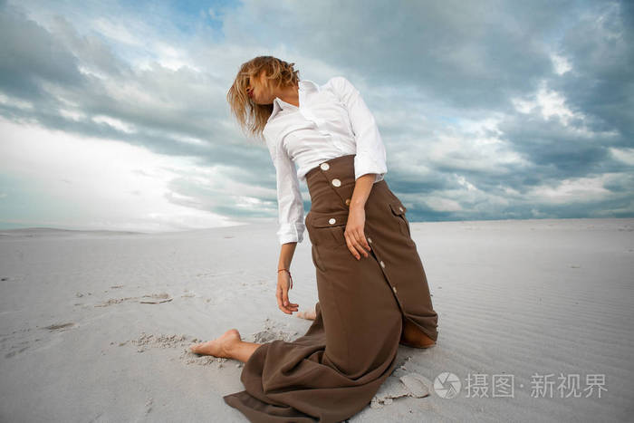 年轻的伤心女人跪在沙漠上天空背景