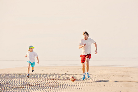 快乐的父亲和儿子踢足球或橄榄球在沙滩上
