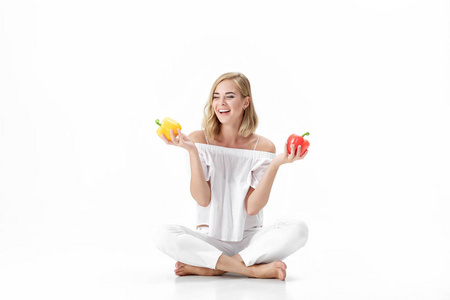 漂亮的金发女郎在白色的衬衫，拿着黄色和红色甜椒。健康的饮食和饮食