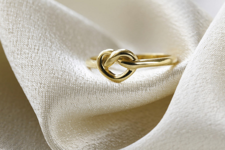 形式的心在米色的丝绸上的金戒指