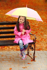 漂亮的小女孩坐在公园长椅上的伞