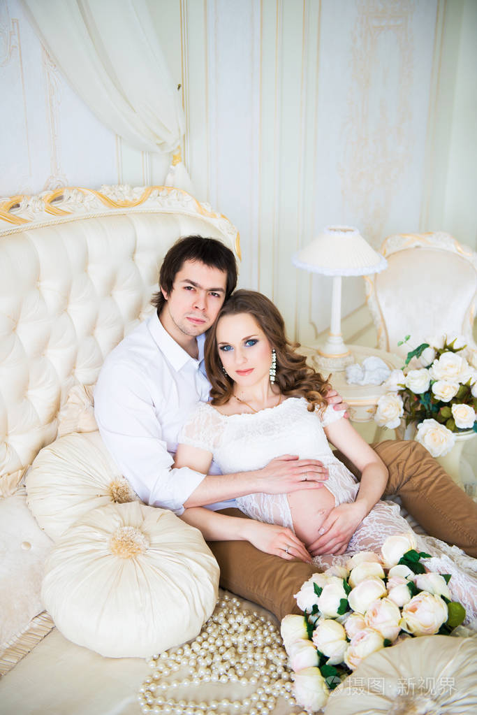 照片 美丽的夫妇,怀孕的年轻女人和男人,拥抱深情地坐在床上,在一个