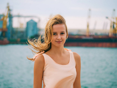美丽的年轻女孩时髦的特写肖像金发与粉红色的嘴唇，微笑着，并在有风的夏季的一天在港口构成