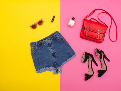 牛仔短裤 鞋子和一个红色的手提包，明亮的黄色和粉红色背景。时尚概念