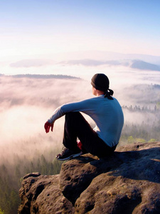男人坐在岩石和观看到多彩雾，雾中森林谷峰