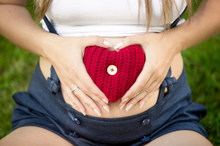 孕妇在胃捧红针织的心的特写
