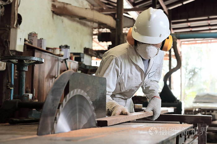 关闭了年轻木材工人在制服和安全设备切割一块木头桌子上锯机在木工
