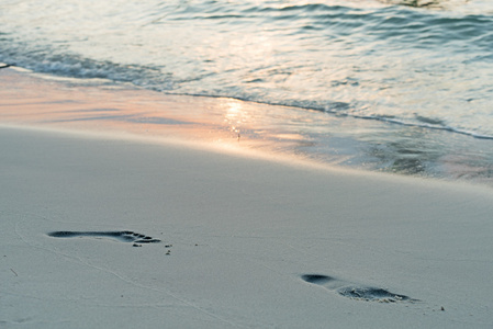 脚印在白色沙子海滩日落背景