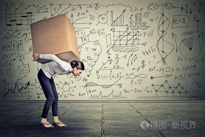 女人背着沉重的箱子走在灰色的墙上