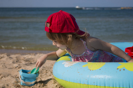 可爱的小女孩戴着红色帽子坐在海滩上一儿童池