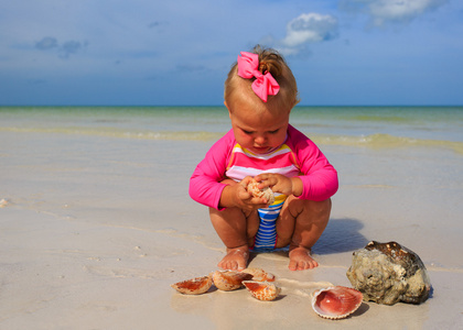 在夏天的海滩上玩着贝壳的小女孩