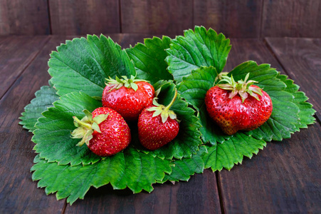 成熟的草莓，绿油油的叶子黑暗的木桌上
