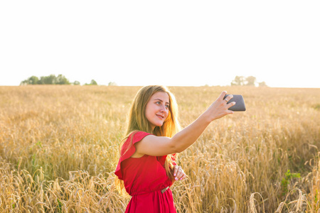 技术 夏季假期，假期和人概念   通过智能手机对谷物场微笑红色连衣裙以自拍照的年轻女子