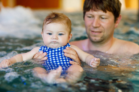 快乐的中年父亲和可爱的可爱宝贝女孩在游泳池里游泳