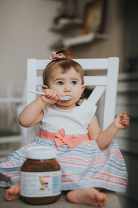 可爱的小宝贝女孩在厨房的桌子上用勺巧克力奶油吃东西和做鬼脸快乐
