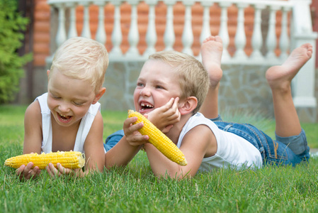 躺在草地上的两个兄弟和吃玉米棒子在花园里